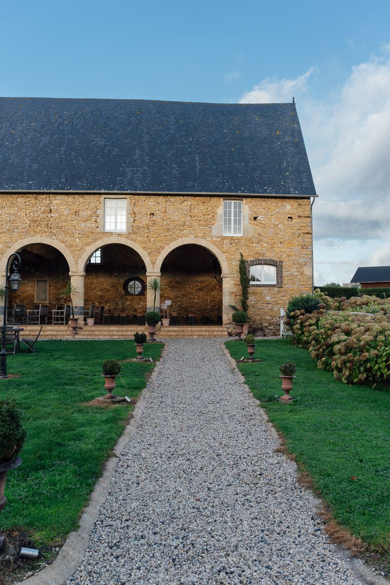 Façade en pierre d'une grange rénovée avec des arches et un chemin en gravier.