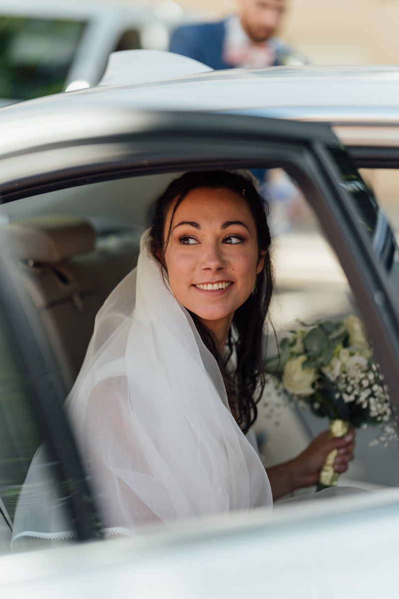 Mariée souriante regardant par la fenêtre d'une voiture avec bouquet de fleurs à la main.