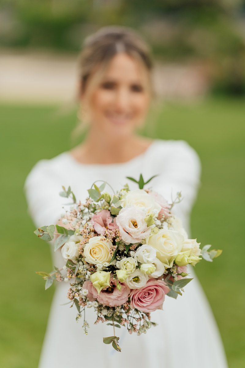 Mariée souriante tenant un bouquet de fleurs variées dans un jardin.