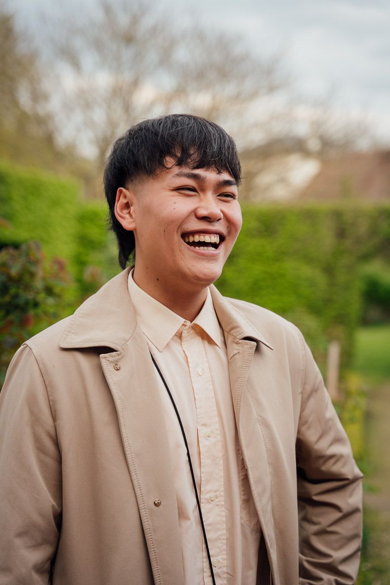 Homme riant dans un jardin avec un manteau beige