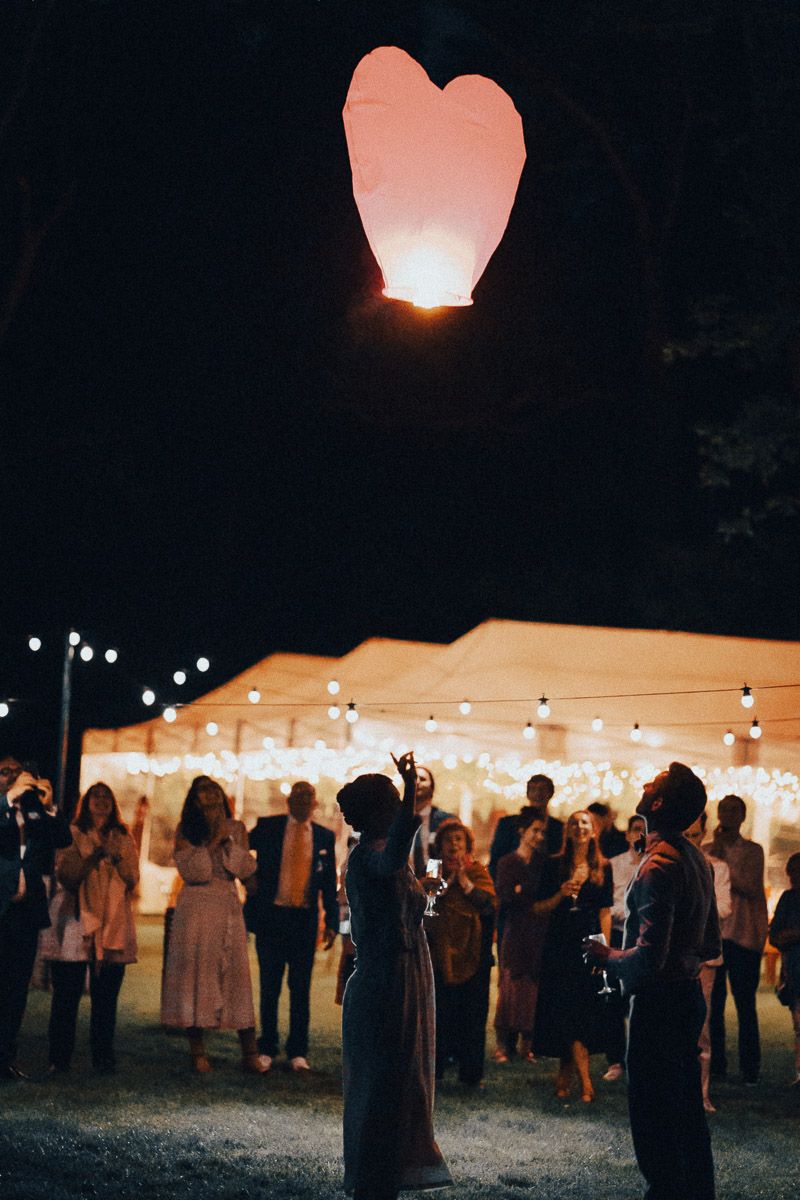 Lâcher de lanterne en forme de cœur lors d'une réception de mariage en soirée.