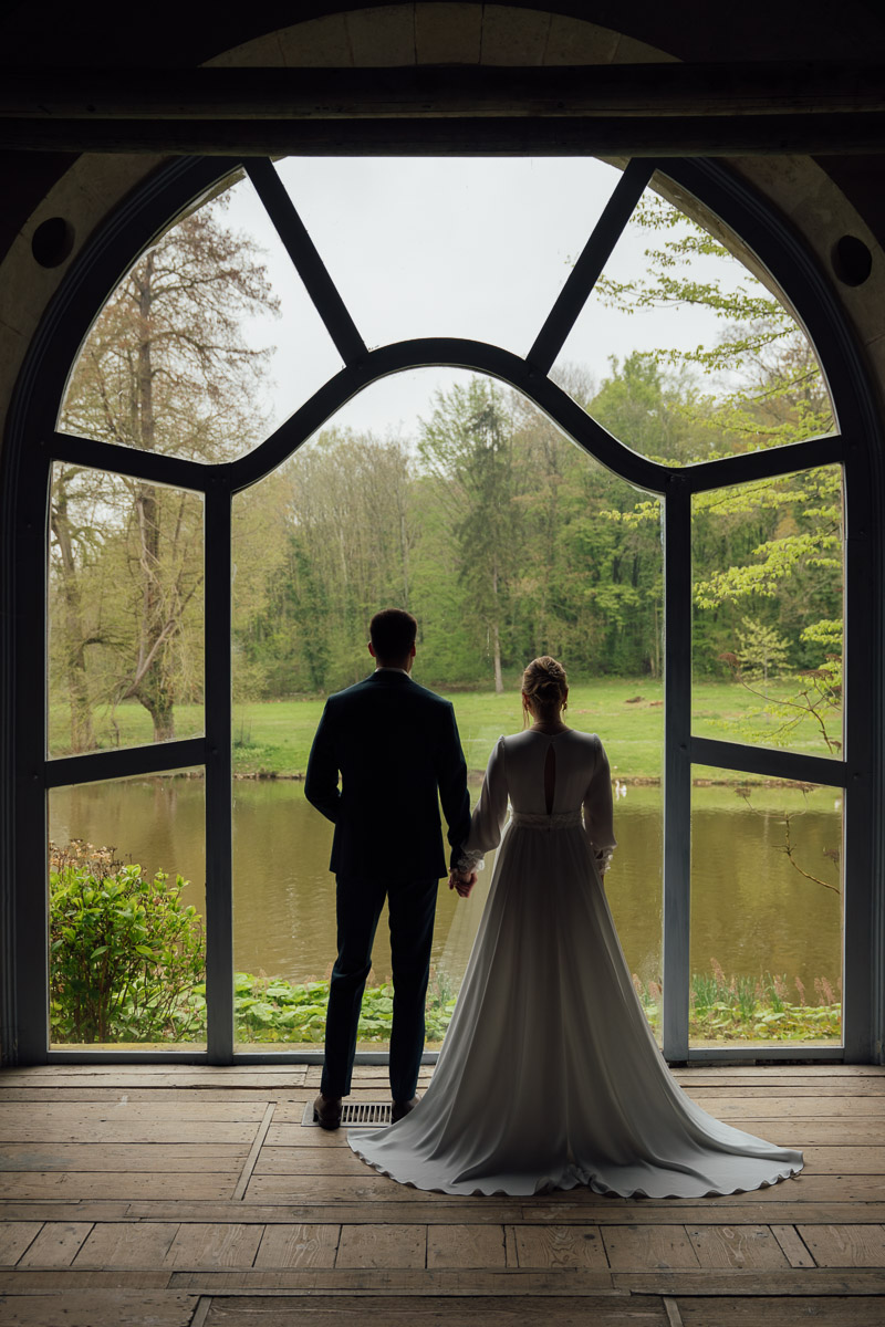 Un couple regardant l’horizon à travers une grande fenêtre encadrée par un paysage naturel.