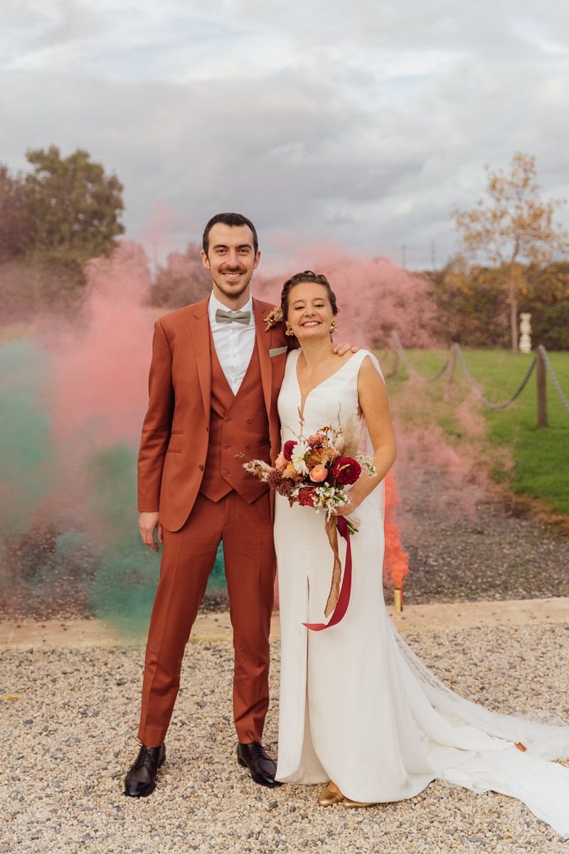 Couple de mariés devant un nuage de fumée rose avec bouquet de fleurs